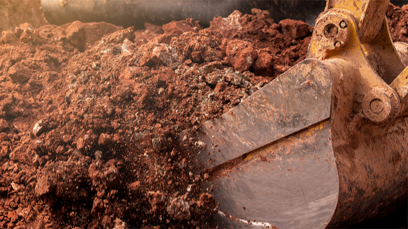 An Excavator Bucket Digging Through Rocky Compacted Soil